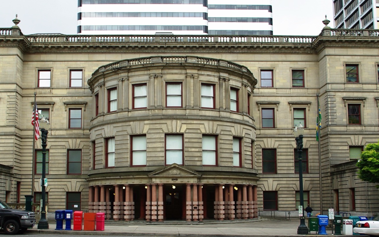 The front of Portland City Hall, a stone building with a columned entrance, seen from across Fourth Avenue.
